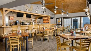 Ein Restaurant mit mehreren Holztischen und -stühlen, einer Bar und Blick durch große Fenster.