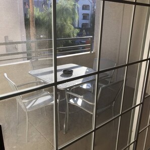 Blick durch ein Fenster mit Metallgitter, einem Tisch und Stühlen.