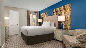 A hotel room with a large bed, two bedside lamps, a patterned carpet, a chair, and a door. - Ideal Las Vegas Villa Near Formula 1 Race Action (Las Vegas)
