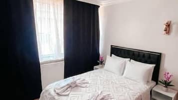 Een hotelkamer met een bed, een nachtkastje, een raam met gordijnen en een klein tafeltje.