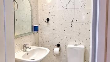 A bathroom with a sink, mirror, toilet, and a trash bin.