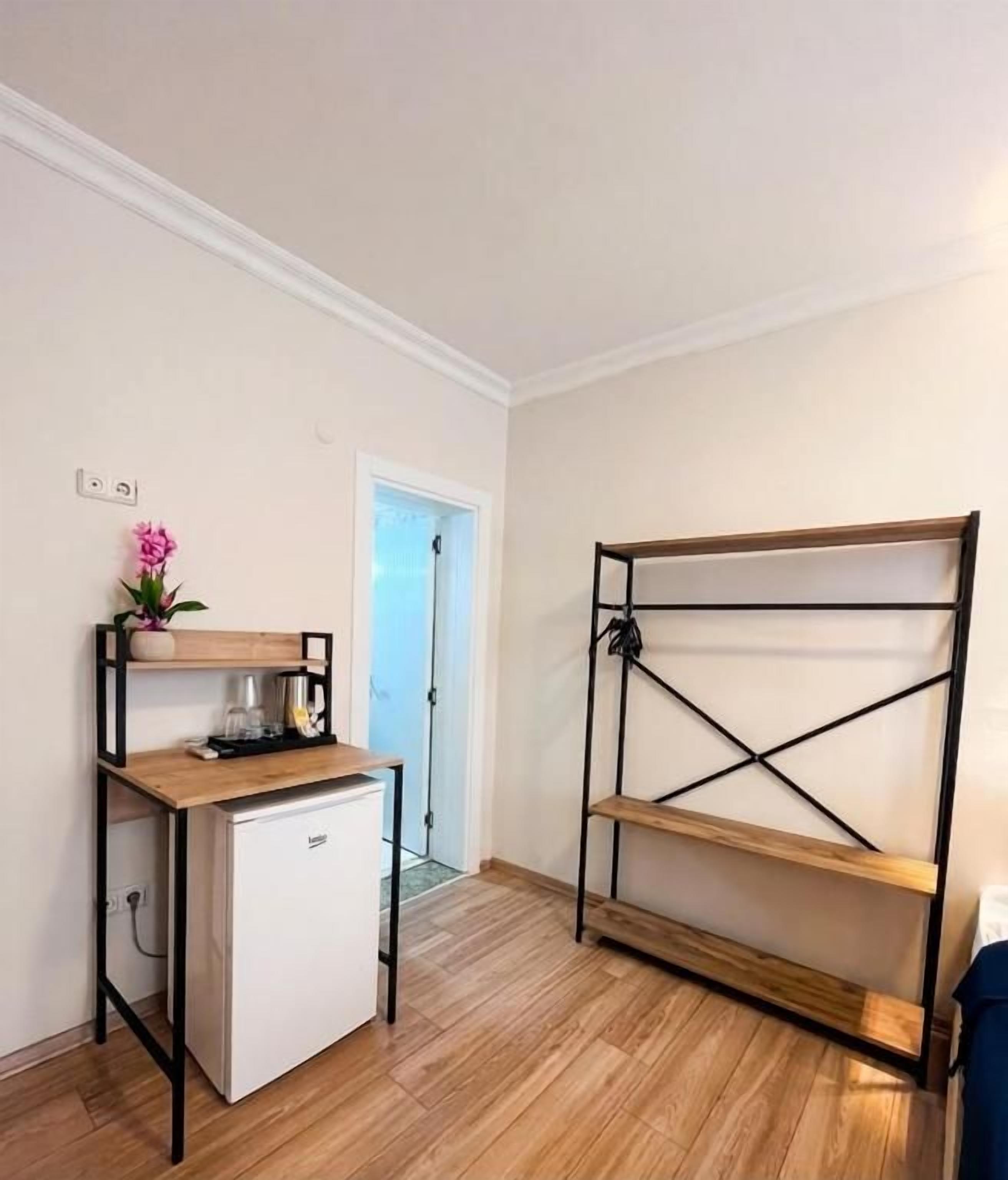 Una kitchenette compacta con un refrigerador pequeño, una estantería de madera y una puerta que da a otra habitación.