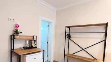 Una kitchenette compacta con un refrigerador pequeño, una estantería de madera y una puerta que da a otra habitación.