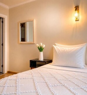 A bedroom with a bed, a bedside table, a vase with flowers, a wall-mounted light, and a mirror.