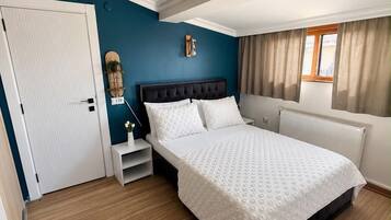 Un dormitorio con cama, una mesita de noche, una lámpara de pared y una ventana con cortinas.