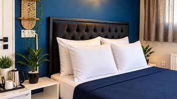 Un dormitorio con pared azul oscuro, cabecera capitonada, ropa de cama blanca y una mesita de noche con cafetera y una planta.