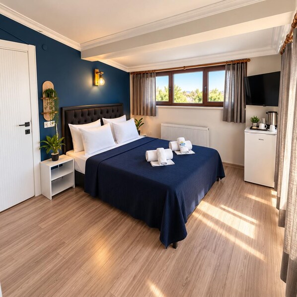 Habitación de hotel con cama, mesita de noche, un pequeño armario blanco, radiador, ventana con cortinas, televisor y refrigerador.