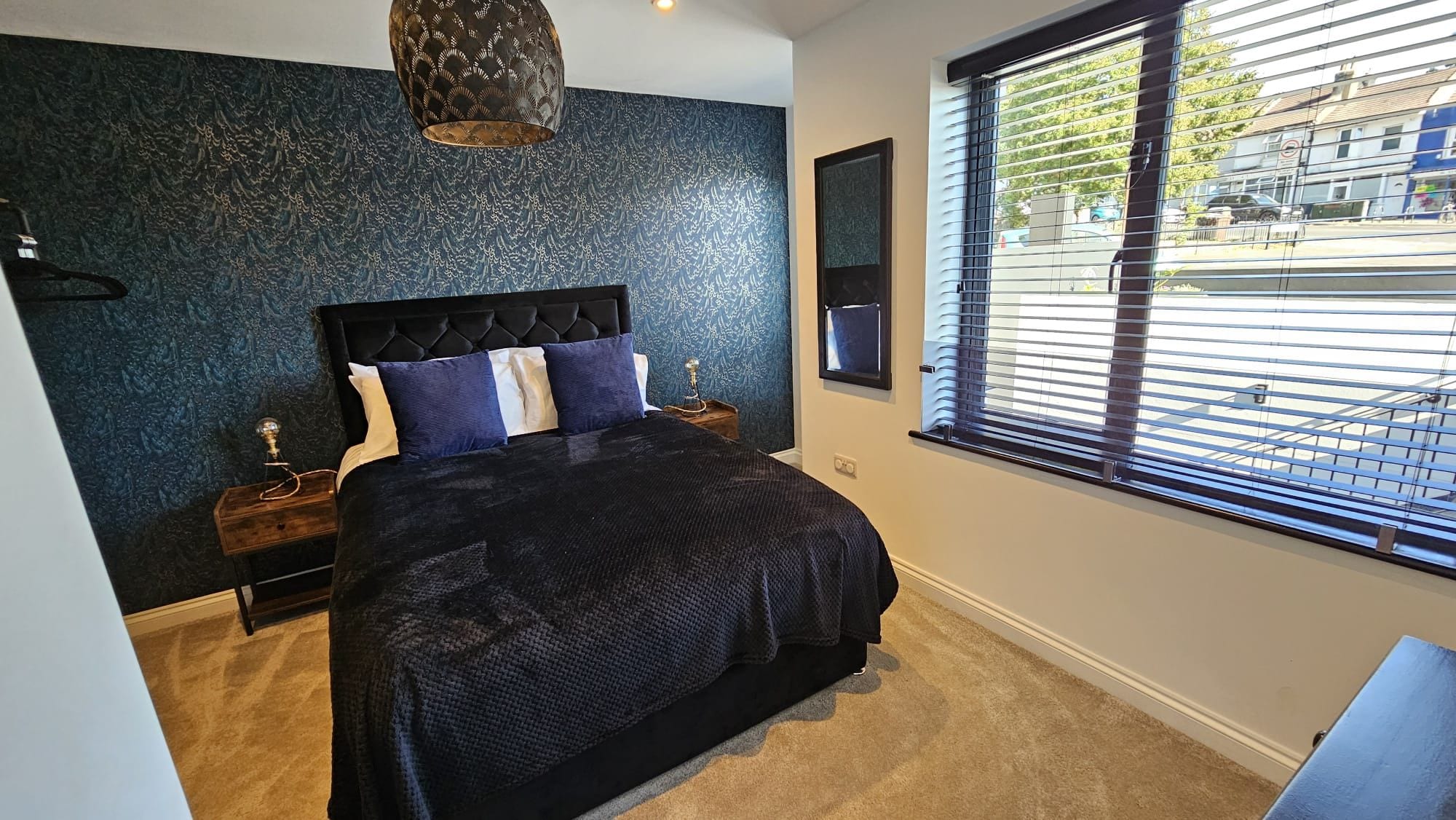 A bedroom with a bed, nightstands, a wall-mounted TV, and a window with blinds.