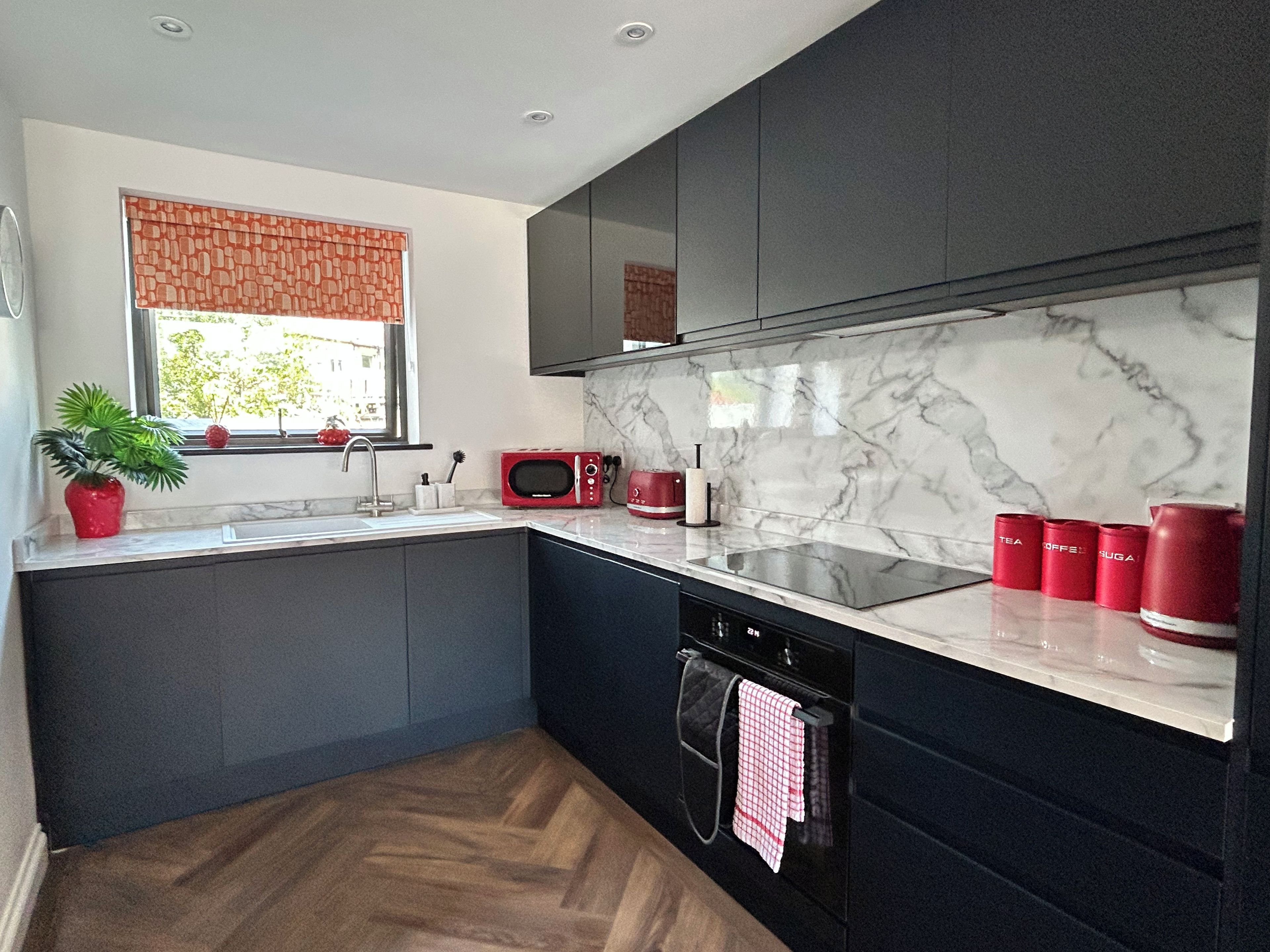 Una cocina moderna con armarios oscuros, encimera de mármol, horno empotrado y ventana con vistas.