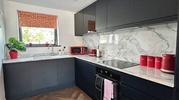 Una cocina moderna con armarios oscuros, encimera de mármol, horno empotrado y ventana con vistas.