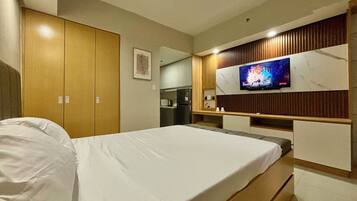 Ein Hotelzimmer mit Bett, Wandfernseher, Holzschrank und einer Küchenzeile.