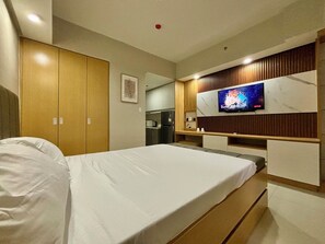 Ein Hotelzimmer mit Bett, Wandfernseher, Holzschrank und einer Küchenzeile.