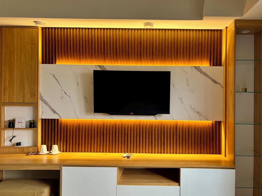 A modern entertainment unit with a flat-screen TV, wooden paneling, and marble accents.