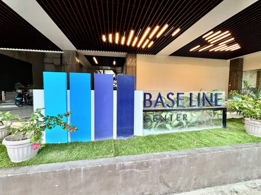 Ein Gebäudeeingang mit einem Schild, auf dem 'BASELINE CENTER' steht, und einer Reihe blauer, vertikaler Strukturen.