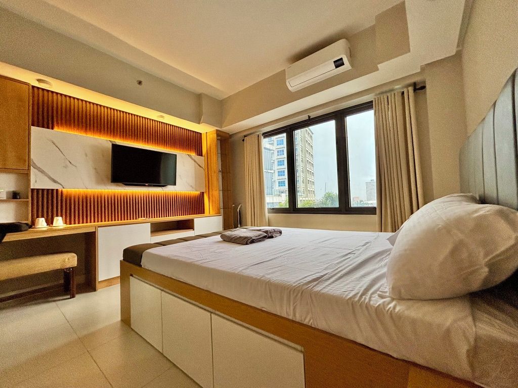 Ein Hotelzimmer mit einem Bett, einem Schreibtisch, einem Flachbildfernseher und einem Fenster mit Vorhängen.