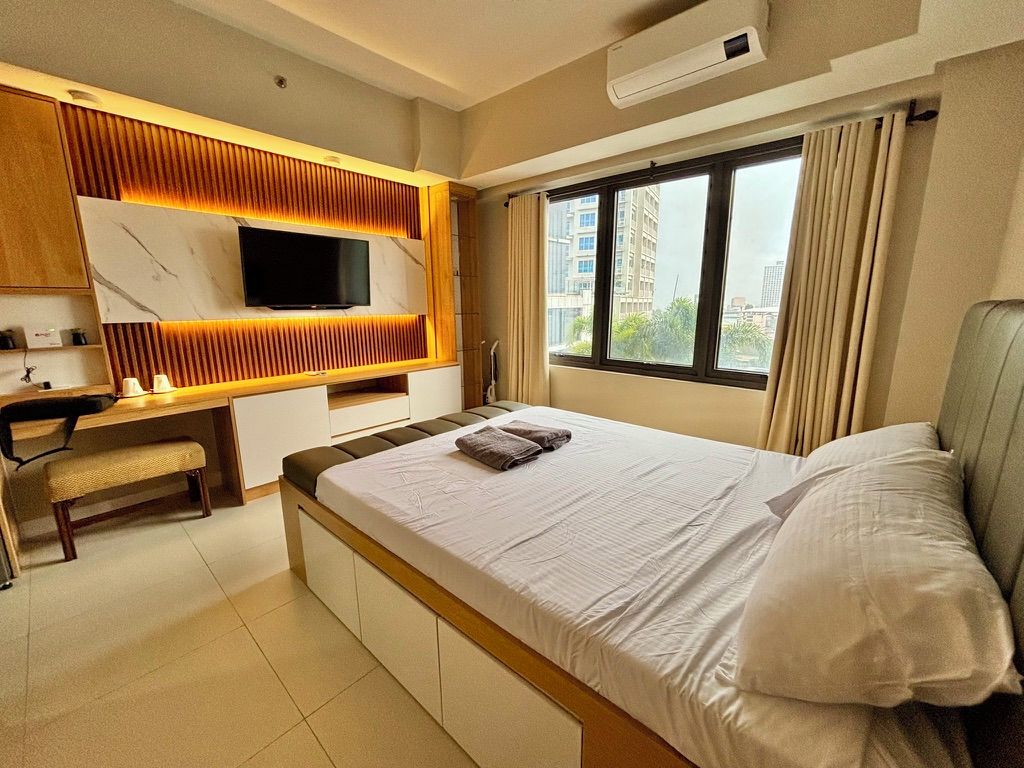 A hotel room with a bed, a desk, a television, and a window with curtains.