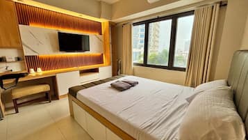 A hotel room with a bed, a desk, a television, and a window with curtains.