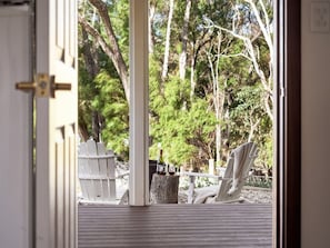Een houten terras met twee Adirondack-stoelen en een fles wijn op een stronk.