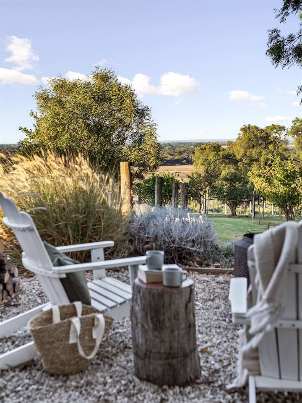 An outdoor seating area with chairs and a table, surrounded by trees and a view of the countryside.
