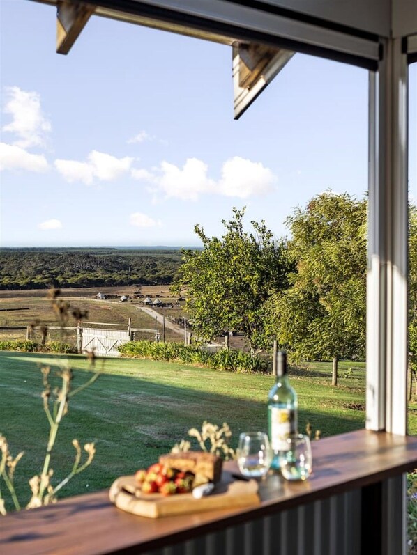A dining area with a view of a rural landscape, a table with food and drinks, and a window overlooking the scenery.