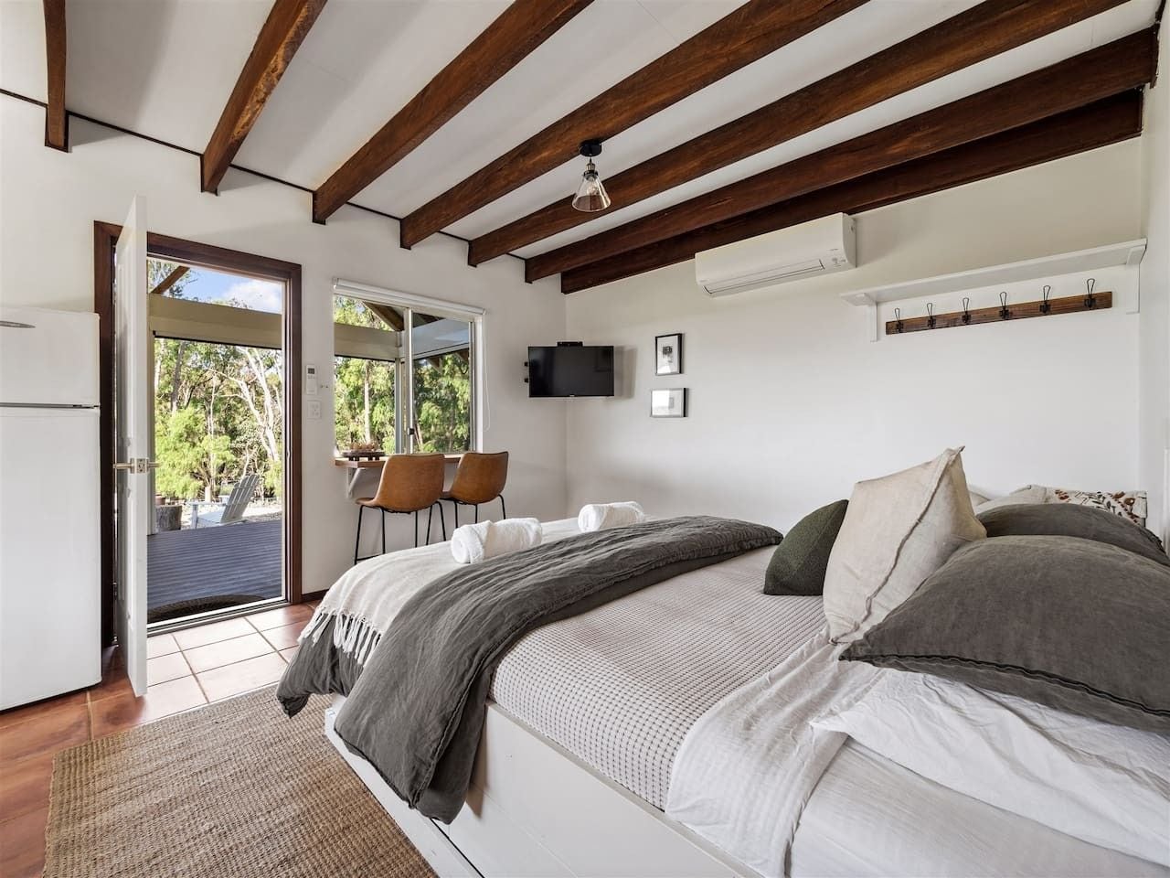 A bedroom with a bed, a desk, and a chair. There is a window and a door leading outside.