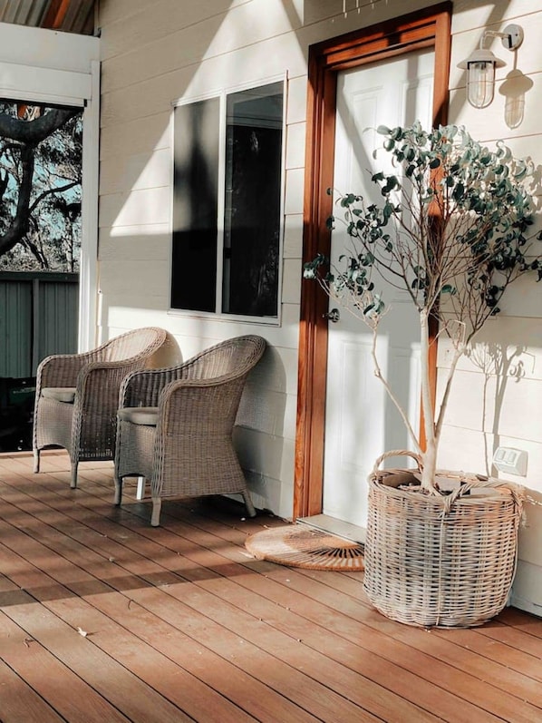 Une véranda couverte avec des fauteuils en osier, une plante en pot et une porte en bois.
