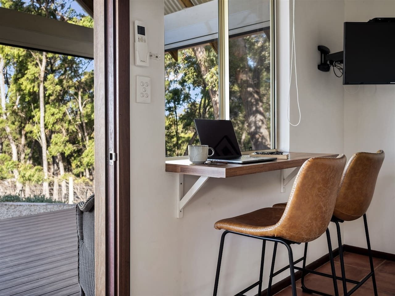 Une pièce comprenant un bureau, deux chaises, un ordinateur portable et une fenêtre donnant sur une zone boisée.