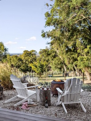 An outdoor seating area with Adirondack chairs, a fire pit, and a bottle of wine on a gravel surface.