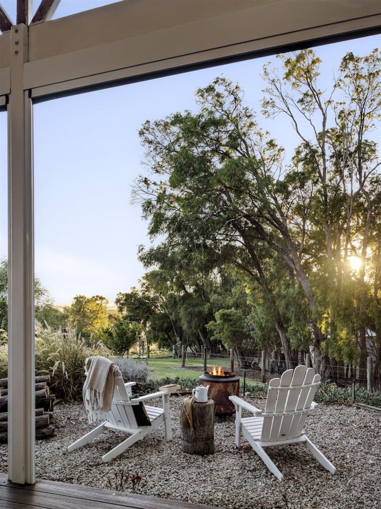 Une terrasse avec deux fauteuils Adirondack, un foyer extérieur et une vue sur une zone boisée.