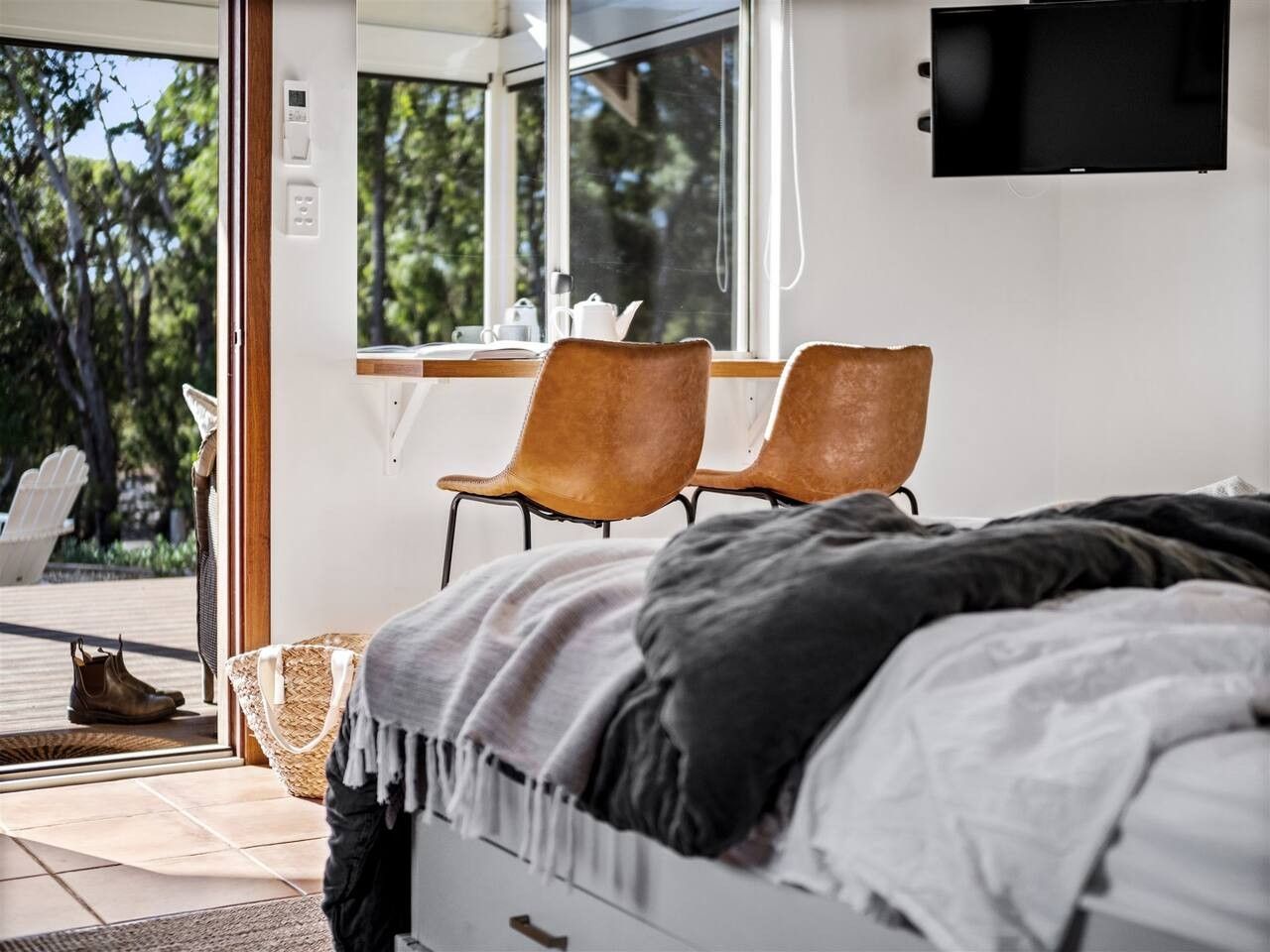 A bedroom with a bed, two chairs, a TV, and a view of the outdoors.