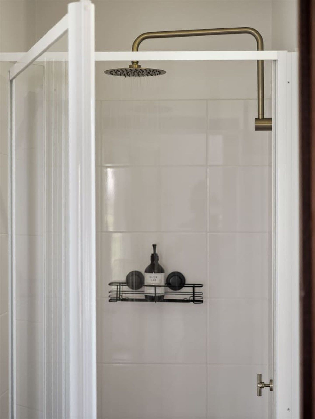 A shower enclosure with a white door, a showerhead, and a shelf with toiletries.