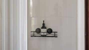 A shower enclosure with a white door, a showerhead, and a shelf with toiletries.