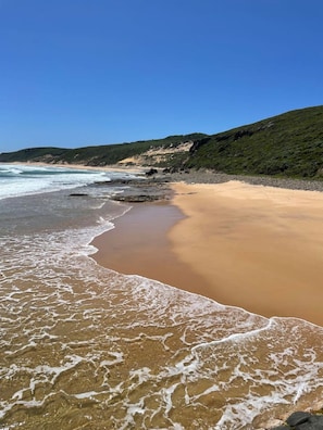 A beach with waves, a sandy shore, and green hills in the background. - Cottage at Dunmore Homestead | Peaceful Retreat (Scott River East)
