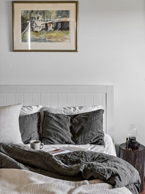 A bedroom with a bed, pillows, a bedside table with a lamp, and a framed picture on the wall.