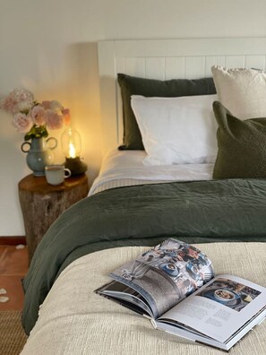 Un lit bien fait, recouvert d’une couverture verte, avec un oreiller blanc et un autre oreiller vert foncé. Un magazine est ouvert sur le lit.