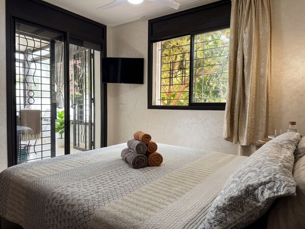 Une chambre d’hôtel avec un lit, un téléviseur fixé au mur, une fenêtre avec des rideaux et une vue sur la verdure.