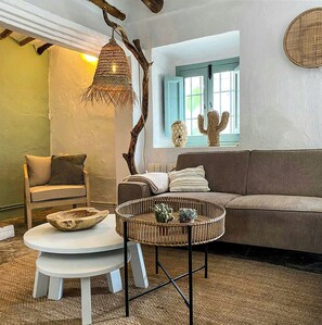 Ein gemütliches Wohnzimmer mit einer Couch, einem Sessel, einem runden Korbtisch und einer Pendelleuchte.