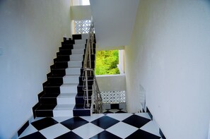 Una scala con pavimento a scacchi bianchi e neri che conduce a una finestra vista su del verde.