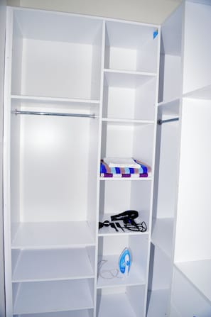 A white wardrobe with multiple shelves and hanging space, including a metal rod and a blue iron. - The Coastal Nest Diani Beach (Diani Beach)