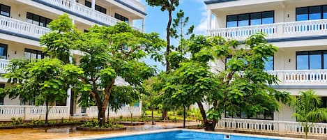 A swimming pool with a clear blue sky, surrounded by multi-story buildings with balconies.