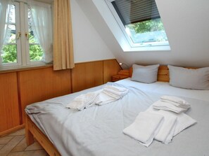 A bedroom with a sloped ceiling, a bed with white linens, a nightstand, and a window with curtains. - Gmelinstrasse 19 d (Wyk auf Foehr)