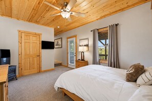 Une chambre à coucher avec un lit, un ventilateur de plafond, une télévision et une fenêtre avec des rideaux.
