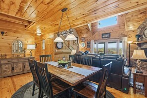A wooden cabin interior with a dining area, a fireplace, and a view of the outdoors. - Deer Mountain Retreat: Mountain Views: Hot Tub (Ellijay)