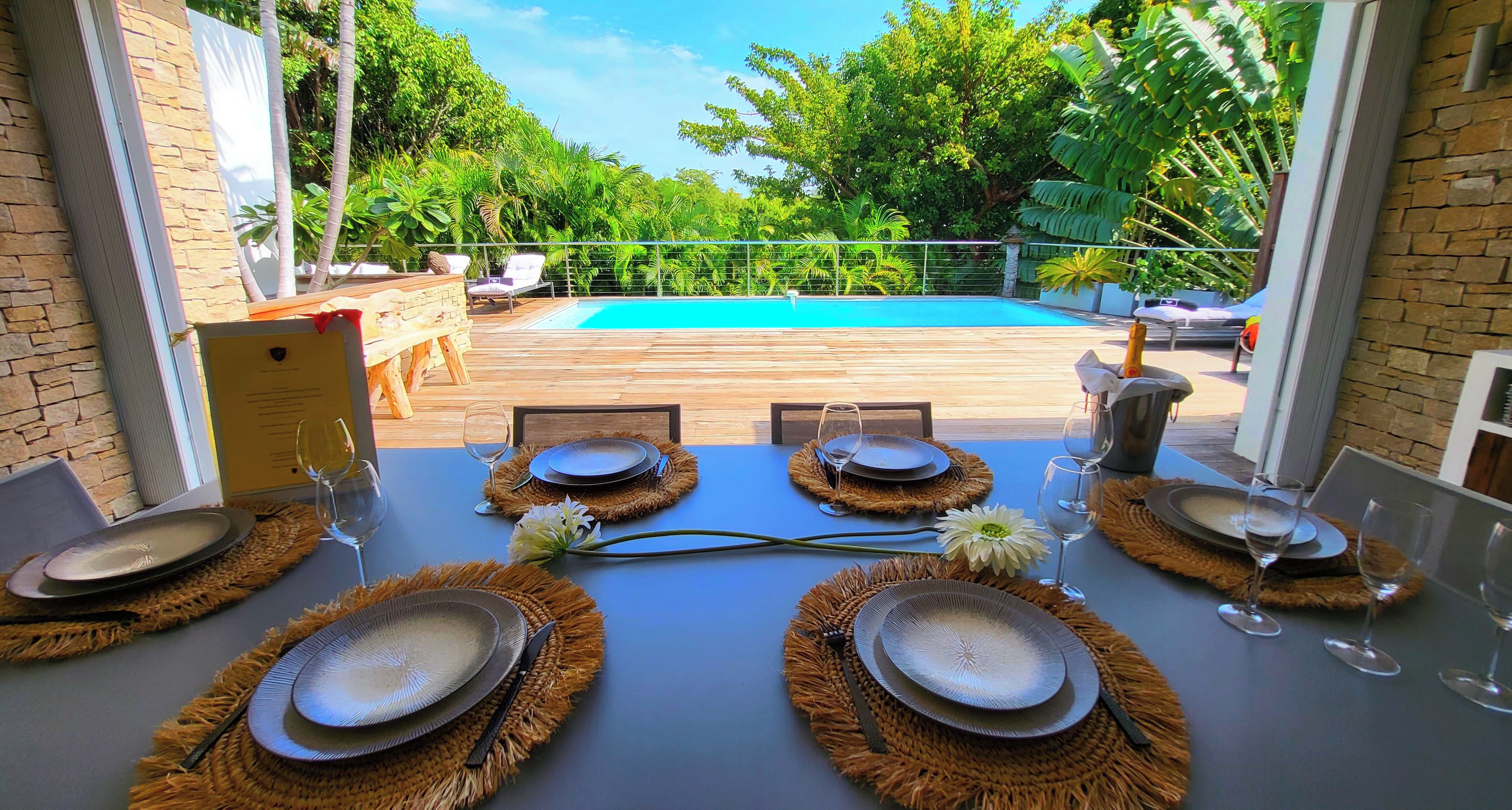 An outdoor dining area with a view of a swimming pool, surrounded by lush greenery.