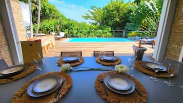 An outdoor dining area with a view of a swimming pool, surrounded by lush greenery.