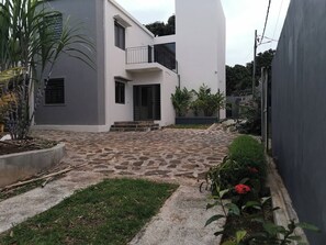 Ein modernes, zweistöckiges Gebäude mit einem gepflasterten Innenhof, einer kleinen Gartenanlage mit Pflanzen und Blumen sowie einer grauen Außenwand.