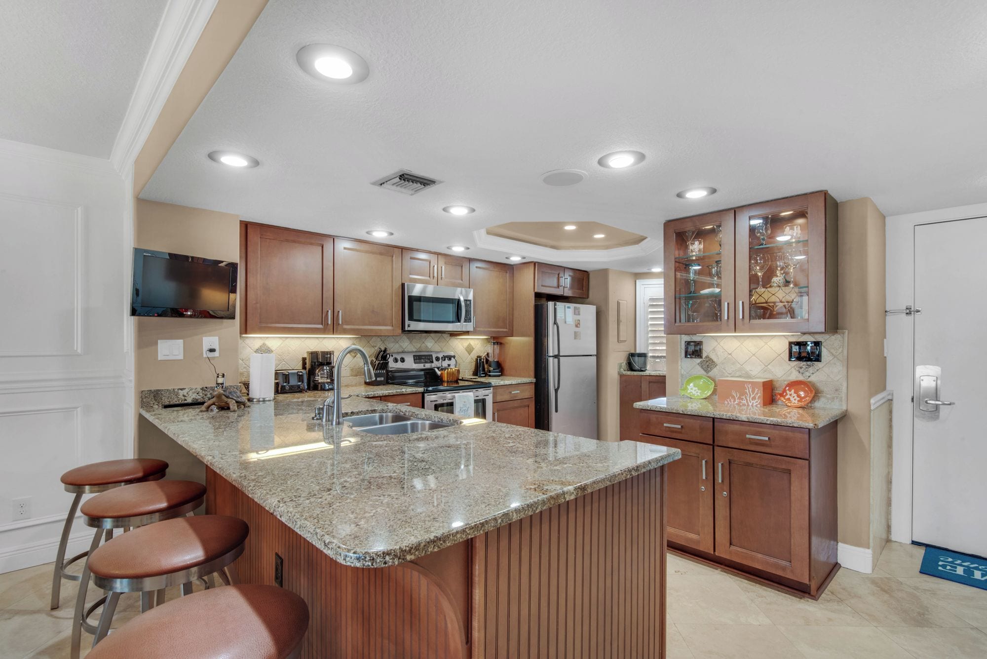 A modern kitchen with granite countertops, stainless steel appliances, wooden cabinets, and a bar area with stools.