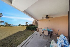 A balcony with a table and chairs, a ceiling fan, and a view of the ocean and palm trees. - Edgewater Beach Condo 202 (Destin)