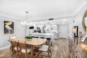 Eine moderne Küche mit weißen Schränken, einer zentralen Kochinsel und einem Essbereich mit einem Holztisch und Stühlen.
