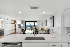 A modern kitchen with a central island, a dining area with a view, and a living space with artwork. - Edgewater Beach Condo 505 (Destin)